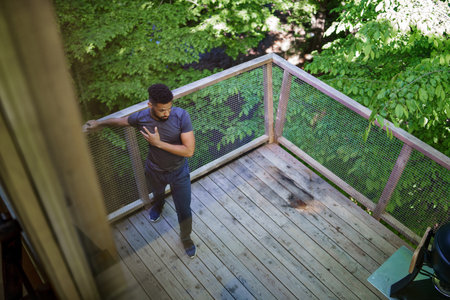 High angle view of happy young man doing exercise outdoors on terrace of tree house, weekend away...