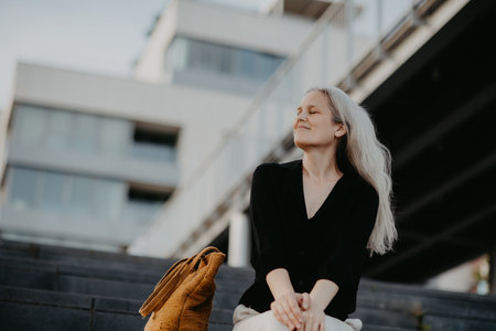Portrait of a beautiful woman with gray hair sitting on concrete stairs in city, enjoying warm summer weather.の写真素材