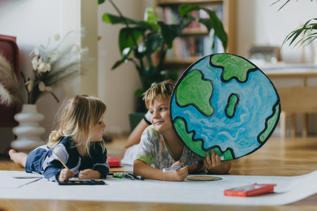 Siblings lying on stomach and painting at home with watercolors and tempera paints, creating a model of planet Earth.の写真素材