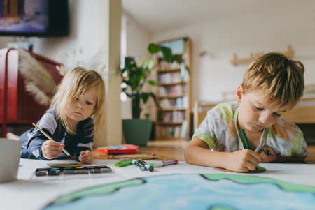 Siblings lying on stomach and painting at home with watercolors, markers and tempera paints, creating a model of planet Earth.の写真素材