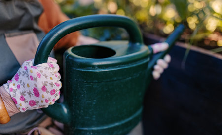 The gardeners hands in gloves holding a plastic watering can.の写真素材
