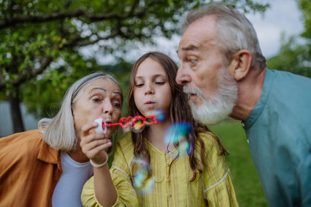 Grandparents and granddaughter are blowing bubbles from a bubble wand.の写真素材