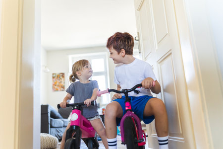 Siblings are riding bicycles indoors, in the hallway of the house.の写真素材
