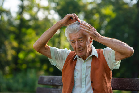 Senior man sitting on a bench in the park and combing his hair.の写真素材