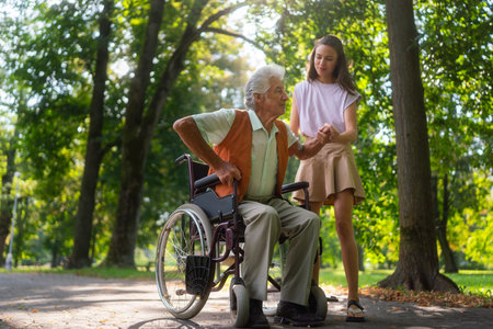 Granddaughter helping the grandfather stand up from the wheelchair.の写真素材