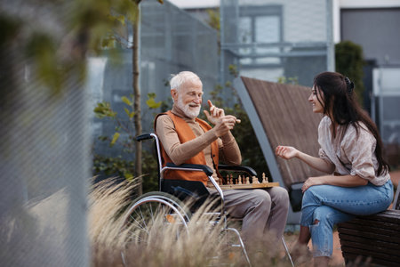 Senior man playing chess outdoors with his daughter.