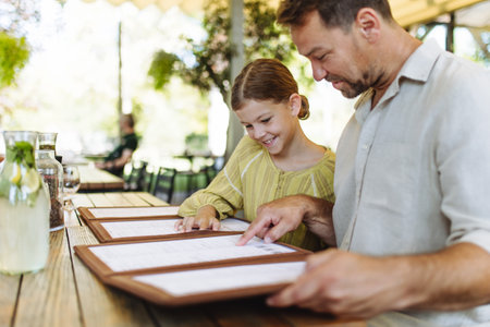 Father and daughter reading menus in a restaurant, choosing food and drinks.の写真素材