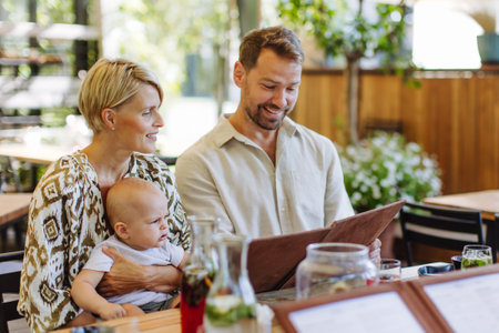 Family with baby reading menu in a restaurant, choosing food and drinks.の写真素材