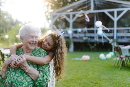Young girl hugging her elderly grandmother at a garden party.の写真素材