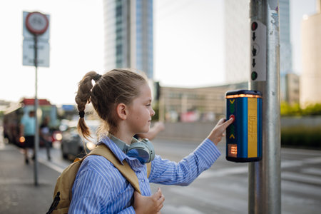 Schoolgirl standing at the crosswalk and pressing the crosswalk button.
