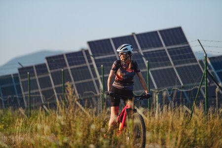 Beautiful cyclist riding in front of solar panels at a solar farm.