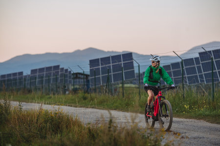 Female cyclist riding in front of solar panels at a solar farm.