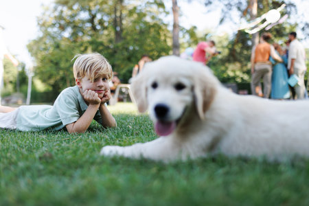 Children playing with a small puppy at a family garden party. Portrait of little boy lying on grass with Golden retriever puppy.の写真素材