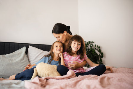 Mother with two daughters on a bed in the bedroom. Fatherless family sit and hug each other. Concept of Mothers Day and maternal love.の写真素材