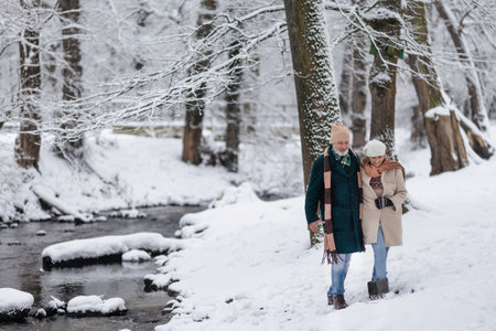 Elegant senior couple walking in the snowy park, during cold winter snowy day. Elderly couple spending winter vacation in the mountains. Wintry landscape.の写真素材