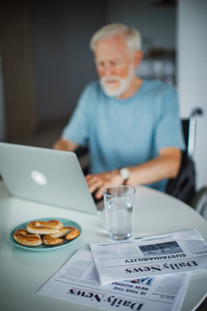 Senior man in a wheelchair shopping online on laptop. Elderly man using digital technologies,...