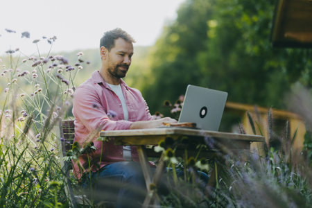 Low angle shot of man working outdoors in the garden, with laptop on legs. Businessman working remotely from homeoffice, thinking about new business or creative idea.の写真素材