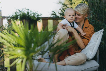 Beatiful mother sitting with little son outdoors, in garden patio. Warm autumn day of mother with...