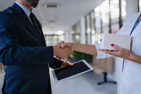 Pharmaceutical sales representative shaking hand with female doctor in medical building. Hospital director consulting with healthcare staff.の写真素材