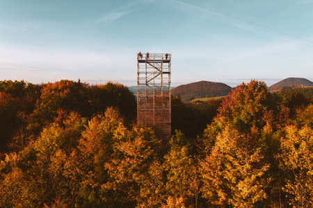Aerial view of a wooden lookout tower in autumn nature. People stand on the observation tower, enjoying the beautiful, serene view of the surrounding landscape.の写真素材