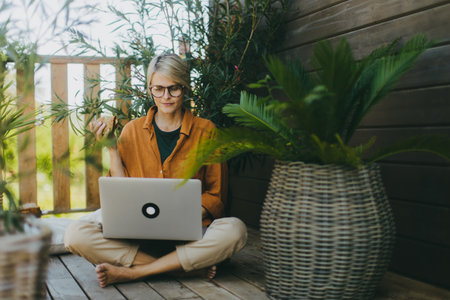 Woman working on laptop while eating sandwich. Businesswoman working remotely from outdoor homeoffice, having light lunch in the garden. Concept of outdoor home office.の写真素材