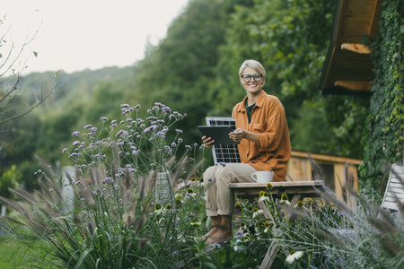 Woman in garden holding solar panel and tablet. Looking for solar panels grants, funds for homeowners. Solar energy and sustainable lifestyle for family in house.の写真素材