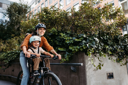 Mother carring her son on a child bike carrier, seat, both wearing helmets. Mom commuting with a young child through the city on a bicycle.の写真素材