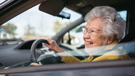 Happy senior woman driving car alone, enjoying car ride. Safe driving for elderly adults, older driver safety.の写真素材