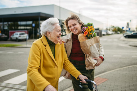 Mature granddaughter carrying grandmothers shopping bag. Senior woman and caregiver going to home with groceries from supermarket, during cold autumn day.の写真素材
