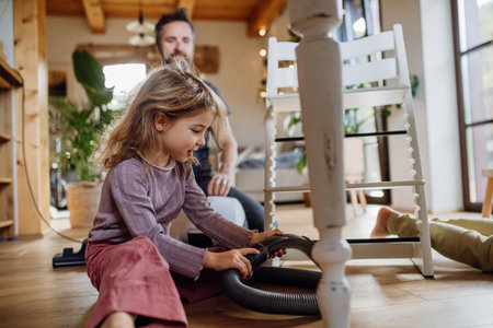 Young girl vacuuming floors with a vacuum cleaner. Father and daughter cleaning the house, helping with house chores.の写真素材