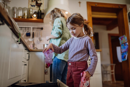 Girl throwing plastic bottles into recycling bin. Daughter sorting the waste according to material into colored bins.の写真素材
