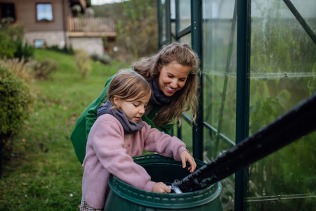 Girl and mother scooping rainwater from barell under downspout. Concept of water conservation in garden.の写真素材