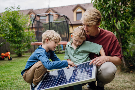 Father and his sons holding solar panel in the garden, learning about photovoltaics and green energy.の写真素材