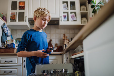 Boy helping to load dishwasher after breakfast. Cleaning the kitchen before leaving to school. Family morning routine.の写真素材