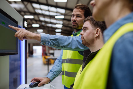 Young man with Down syndrome working in warehouse, colleague teaching him work with computer....