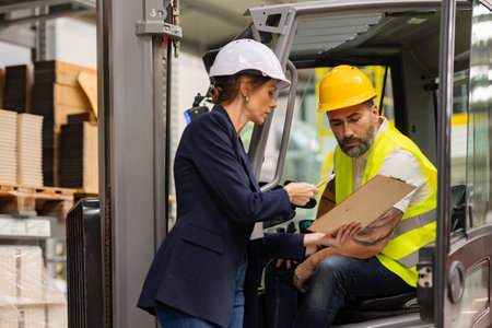 Forklift driver talking with manager in modern industrial factory. Warehouseman reading order, order picking. Warehouse worker preparing products for shipmennt, delivery, checking stock in warehouse.の写真素材