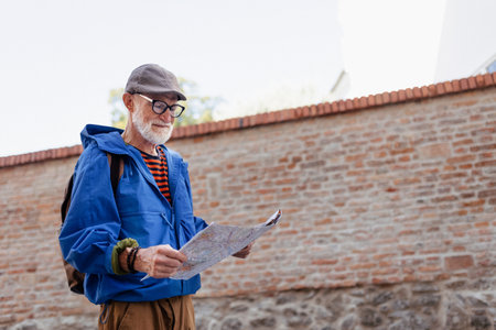 Senior tourist exploring new city, interesting places. Elderly man holding paper map, looking for...