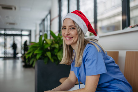 Beautiful nurse with christmas hat sitting in hospital waiting room, corridor. Obstetrics nurse working in hospital on Christmas day, Christmas Eve. Female doctor working a Christmas shift and cant be with her family.の写真素材