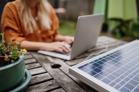 Businesswoman, freelancer or manager working outdoors in garden, garden homeoffice. Remote work from backyard. Laptop is charging with solar charger. Concept of working remotely.の写真素材
