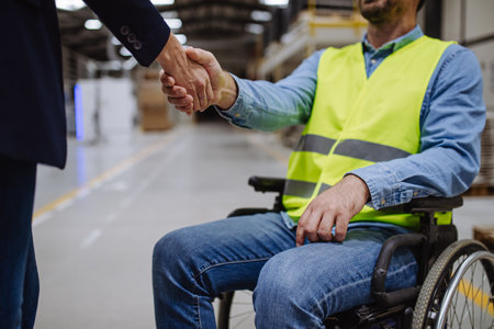 Portrait of man in wheelchair working in warehouse, shaking hand with HR manager, director. Concept of workers with disabilities, accessible workplace for employees with mobility impairment.の写真素材