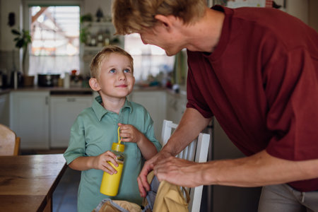 Dad packing school snack for son. Putting juice in bottle and lunch box with healthy snack into his...