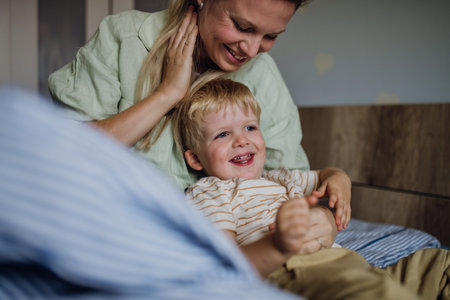 Portrait of little baby boy waking up in the morning. Mother helping son out of bed.の写真素材