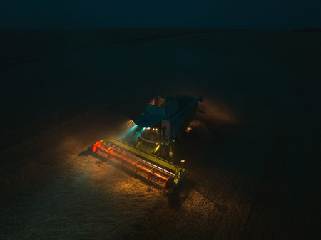 Aerial view of a tractor and harvester working in a field during night. Agriculture and cultivation of industrial farms. Agribusiness.の写真素材
