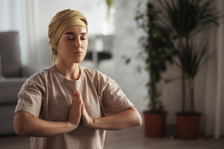 Young woman with cancer taking yoga and meditating in her apartment. Strong female patient calming her mind with easy exercise. Concept of mental health and cancer.の写真素材