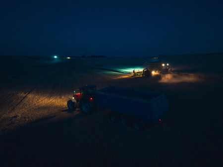 Aerial view of a tractor and harvester working in a field during night. Agriculture and cultivation of industrial farms. Agribusiness.の写真素材