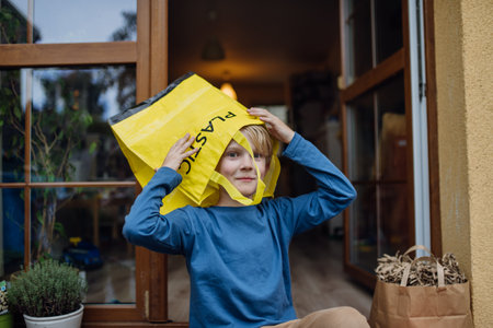 Boy put recycling bag for plastic waste on head. Boy sorting the waste according to material into colored bags.の写真素材