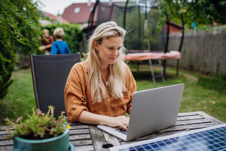 Businesswoman, freelancer or manager working outdoors in garden, garden homeoffice. Remote work from backyard. Laptop is charging with solar charger. Concept of working remotely.の写真素材