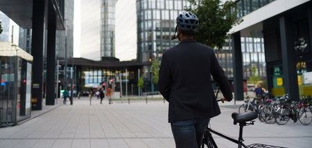 Rear view of city bike commuter leaving work on bicycle after long work day. Banner with copy space.