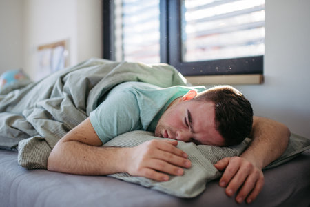 Young man with down syndrome sleeping in his bed. Lying on abdomen, resting in bedroom.