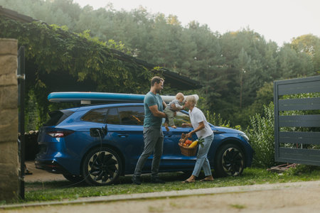 Young family with baby unloading groceries from their electric car. Electric vehicle with charger in charging port.の写真素材